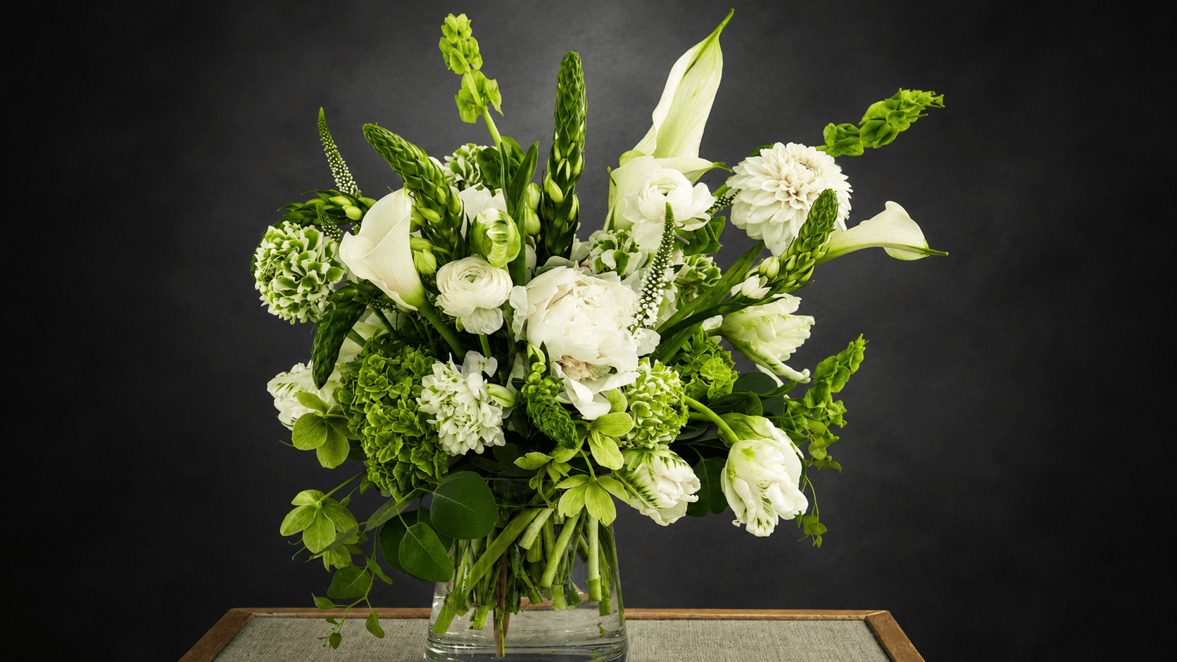 Swann Sympathy arrangement of white lilies, roses and greenery in a glass vase